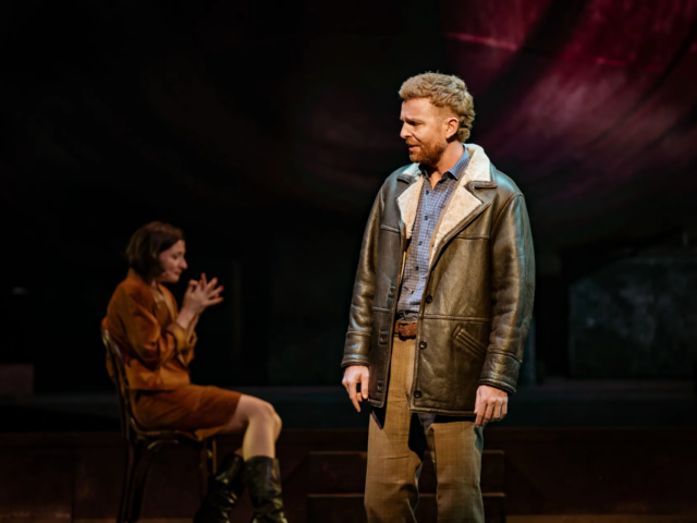 Gideon, in a sheepskin-collared jacket, sings downstage while Meg sits behind him in low light.