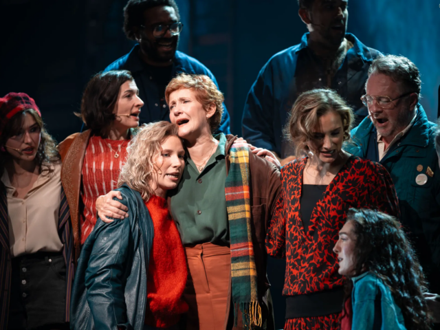The company singing in a tight huddle, Peggy White embracing a younger woman at the centre.