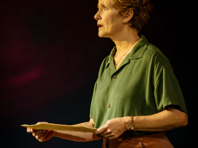 Peggy White holds an open letter at arm's length, singing, tears on her face.