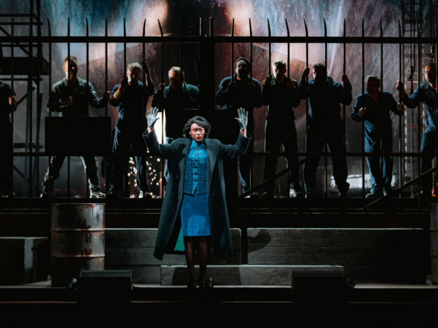 Baroness Tynedale raises both gloved hands as shipyard workers line the railings behind her.
