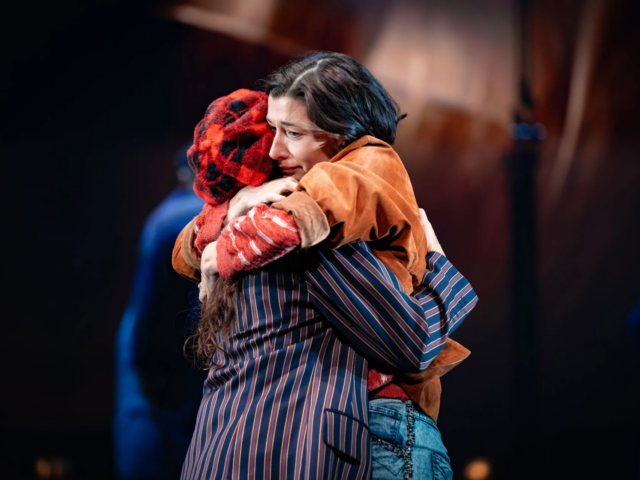 Meg holds a woman in a red tartan beret in a long embrace.