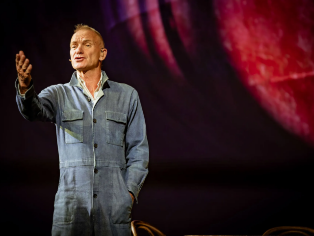 Sting as Jackie White gestures mid-speech in his denim boiler suit.